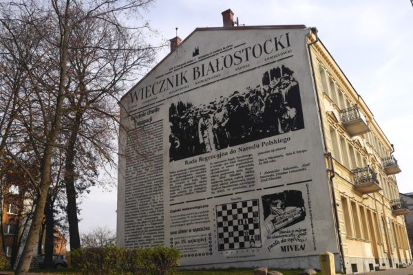 Budynek pokazany stroną szczytową z czarno-białym muralem.