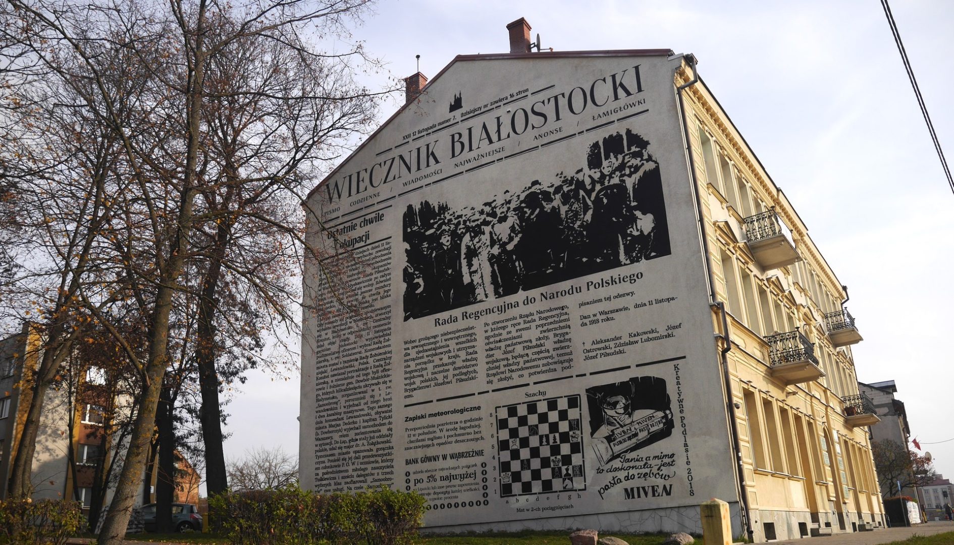 Budynek pokazany stroną szczytową z czarno-białym muralem.