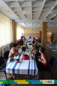 Grupa dzieci siedzących przy stole w trakcie warsztatów wakacyjnych.