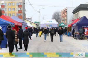 Plac jarmarku po, którym przechadzają się ludzie.