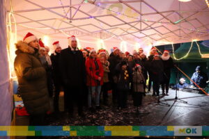 Liczna grupa ludzi śpiewająca na scenie.