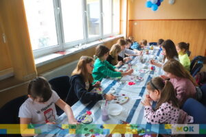 Duża grupa dzieci siedzących przy stole i malująca farbami.