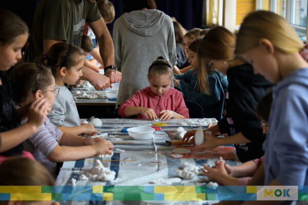 Grupa dzieci przy stołach w trakcie zajęć plastycznych.