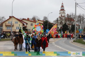 Duża grupa ludzi idąca w orszaku po ulicy na tle kościoła.