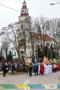 Duża grupa ludzi idąca w orszaku po ulicy na tle kościoła.