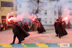 Czterech młodych mężczyzn ubranych na czarno trzyma w rękach odpalone race.