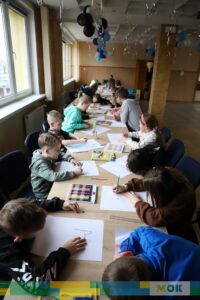 Grupa dzieci przy stołach w trakcie zajęć z rysowania.