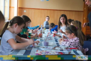 Duża grupa dzieci siedzących przy stole i malująca farbami.