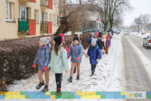 Grupa dzieci idąca zaśnieżonym chodnikiem.
