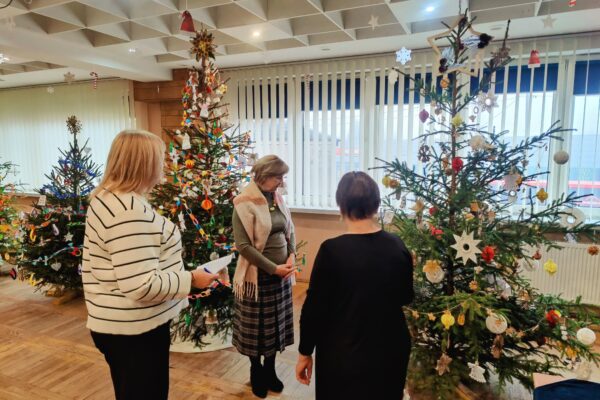 Trzy kobiety stoją wokół choinki w przytulnym pomieszczeniu, ciesząc się świąteczną atmosferą.